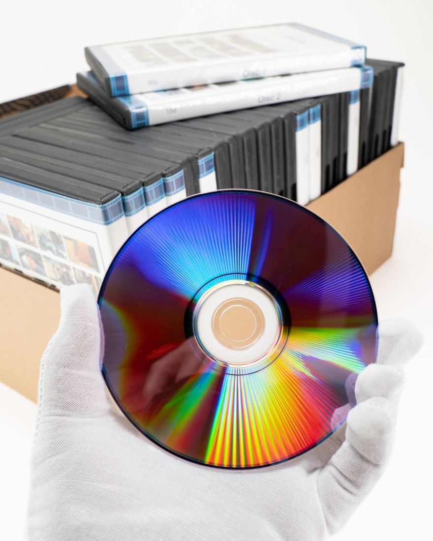 A gloved hand holding a home-burned DVD in front of a box of DVD cases